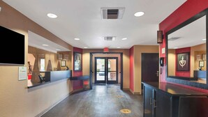 A hotel lobby with a reception desk, a large flat-screen TV, an exit sign, and a phone on the wall. - Extended Stay America Suites San Diego Oceanside (Oceanside)