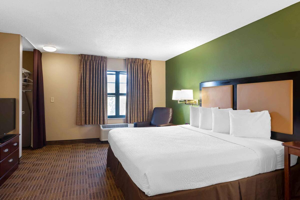 Habitación de hotel con una cama grande, televisión, una silla y ventana con cortinas.