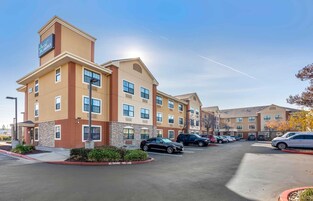 Un hotel de varios pisos con techo plano, una escalera de emergencia y un estacionamiento con varios automóviles.