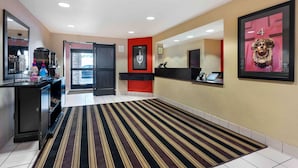 A hotel lobby with a reception desk, a coffee machine, a refrigerator, and a striped carpet.