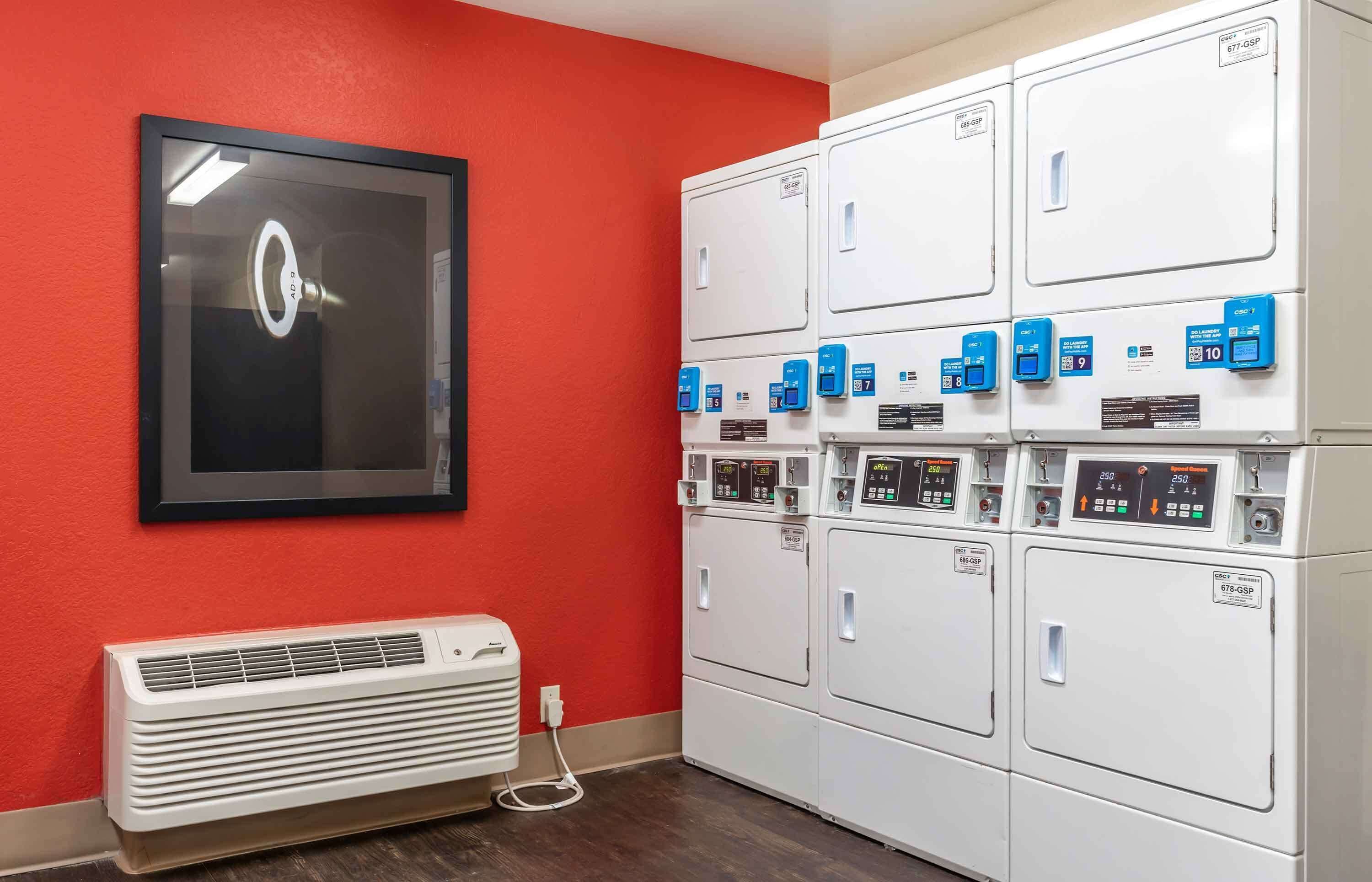 A laundry room with multiple white dryers and a wall-mounted air conditioning unit.