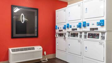 A laundry room with multiple white dryers and a wall-mounted air conditioning unit.