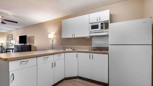 A modern kitchen with white cabinets, a microwave, a refrigerator, and a wooden countertop.