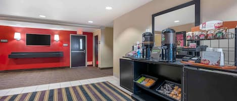 A hotel lobby with a red wall, a reception desk, a coffee station, and a breakfast bar.