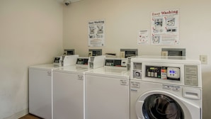 A laundry facility with multiple washing machines and dryers, control panels, and instructional posters on the wall. - HomeTowne Studios By Red Roof Denver - Airport/ Aurora (Aurora)