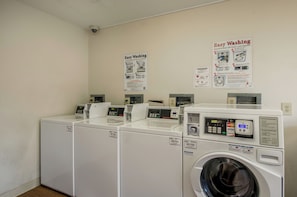 A laundry facility with multiple washing machines and dryers, control panels, and instructional posters on the wall. - HomeTowne Studios By Red Roof Denver - Airport/ Aurora (Aurora)