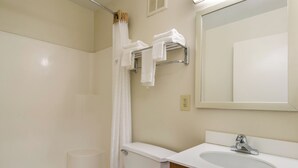 A bathroom with a toilet, sink, and mirror. There is a towel rack with towels and a shower curtain. - HomeTowne Studios By Red Roof Denver - Airport/ Aurora (Aurora)