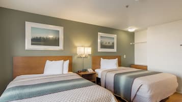Una habitación de hotel con dos camas, una mesita de noche con lámpara y dos cuadros en la pared.