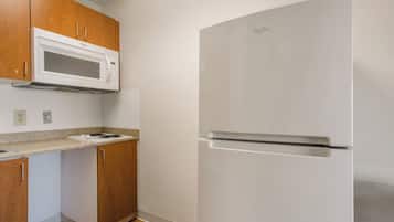 A kitchen with wooden cabinets, a white microwave, a stainless steel refrigerator, and a countertop with a stove.