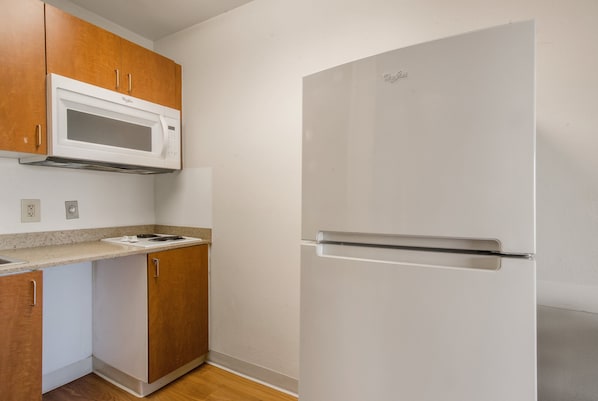 A kitchen with wooden cabinets, a white microwave, and a white refrigerator. - HomeTowne Studios By Red Roof Denver - Airport/ Aurora (Aurora)