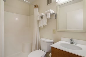 A bathroom with a toilet, sink, mirror, and shower curtain. - HomeTowne Studios By Red Roof Denver - Airport/ Aurora (Aurora)