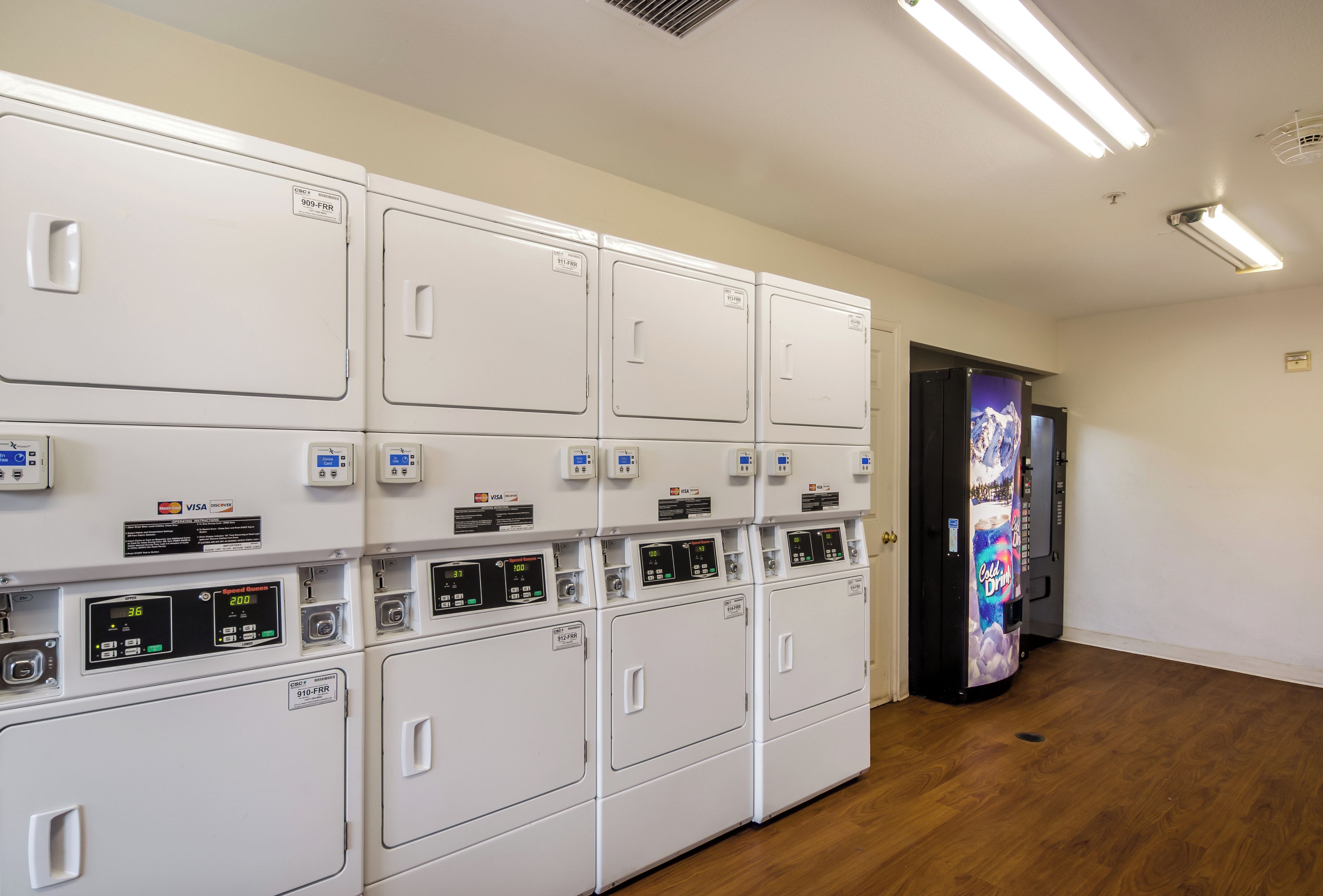 A laundry facility with multiple washing machines and dryers, card payment machines, and a vending machine.