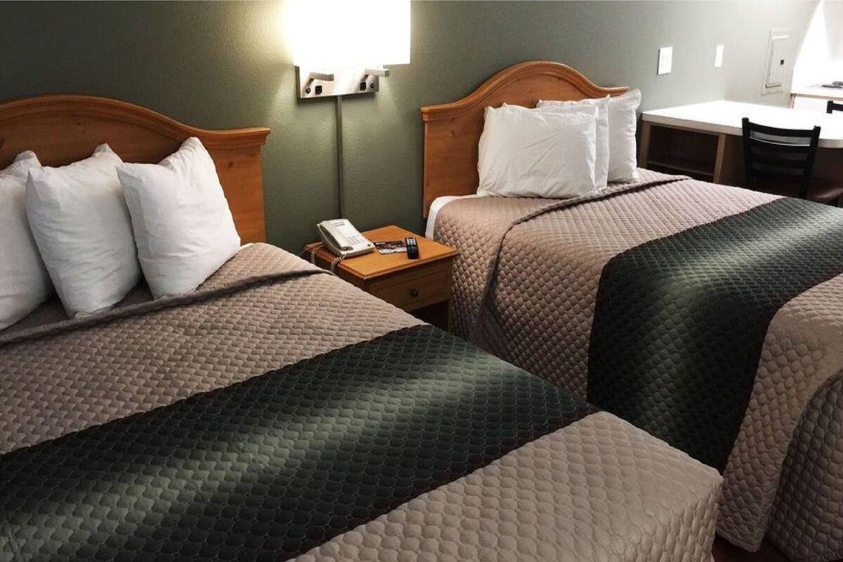 A hotel room with two beds, a desk, and a chair.