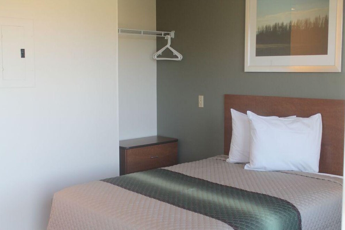 Una habitación de hotel con una cama, una mesita de noche, un perchero y un cuadro en la pared.