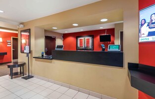 Zona de recepción de un hotel con mostrador, pantalla digital, teléfono y televisor.