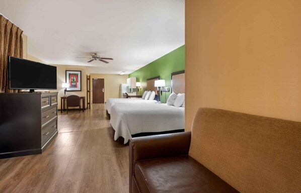 Habitación de hotel con cama, escritorio, televisor y ventilador de techo.