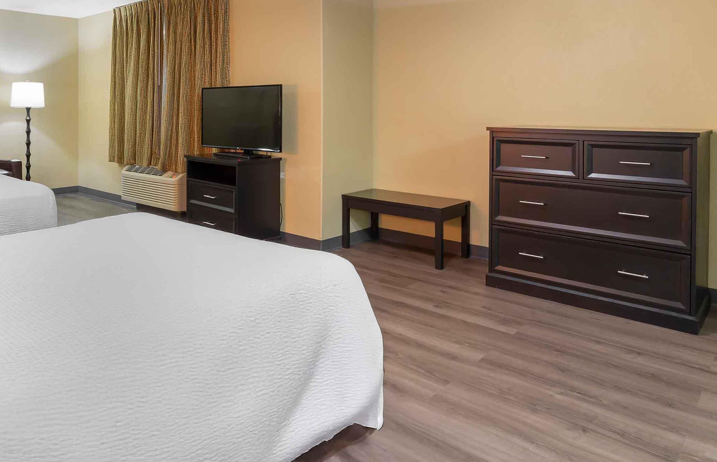 A hotel room with a bed, a television, a dresser, and a small table.