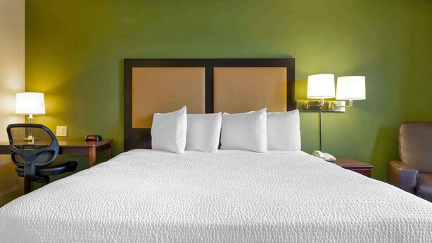 A hotel room with a large bed, two bedside lamps, a desk, a chair, and a telephone.