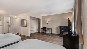 Habitación de hotel con dos camas, un escritorio, una silla, un armario y un televisor.