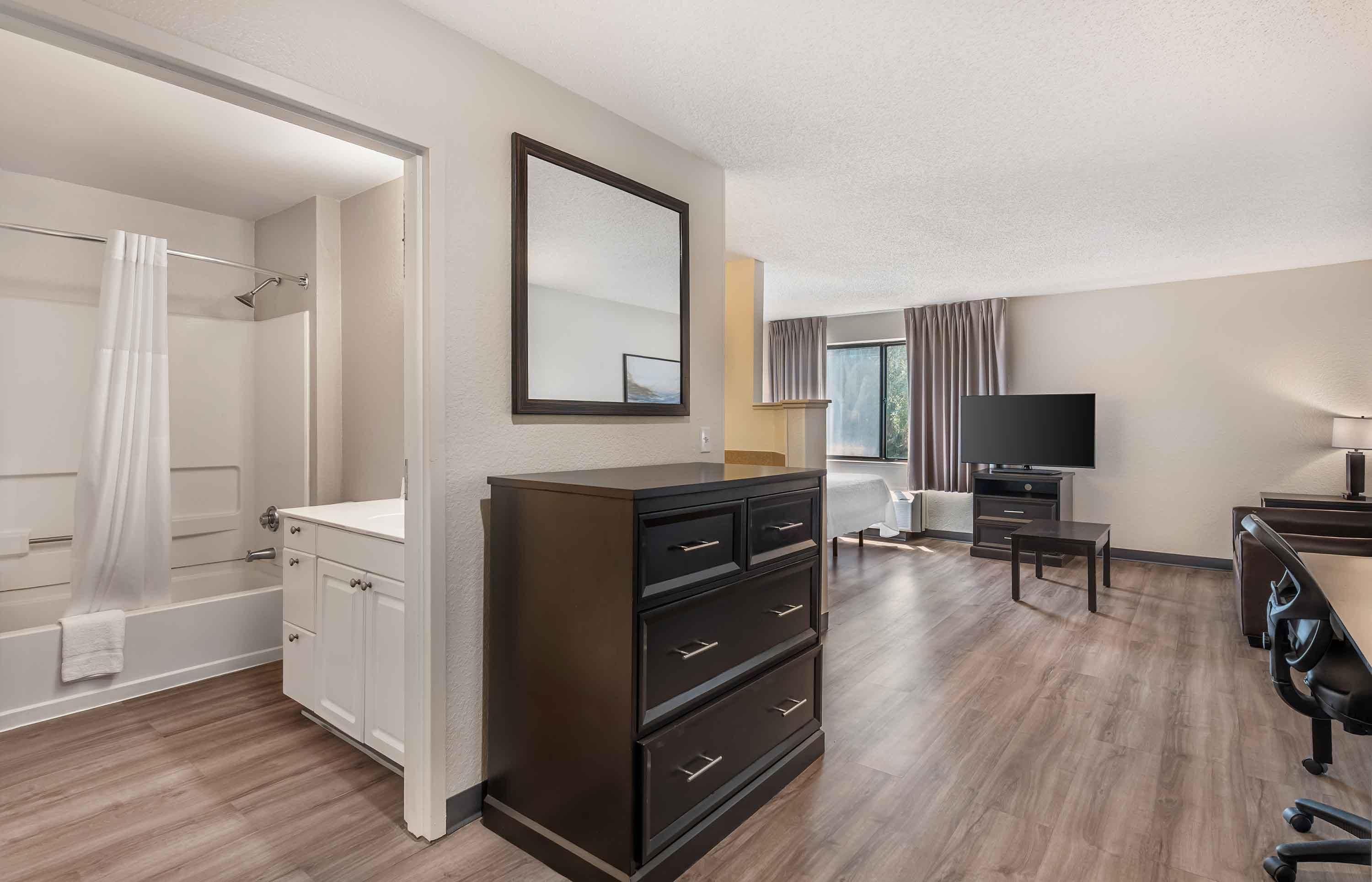 A hotel room with a shower, a dresser, a television, and a desk with a chair.