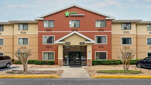 Un hotel Stay America con fachada roja y color beige, entrada al vestíbulo y zona de estacionamiento.