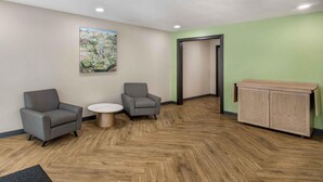 Un espace d’accueil comprenant deux fauteuils gris, une petite table ronde, un meuble en bois et un tableau accroché au mur.