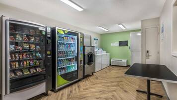 Un ambiente interno pulito e ben illuminato, con distributori automatici, un frigorifero e un tavolo.