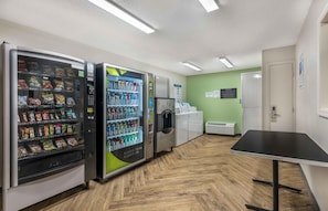 A clean, well-lit indoor space with vending machines, a refrigerator, and a table. - Extended Stay America Suites Daytona Beach Speedway (Daytona Beach)