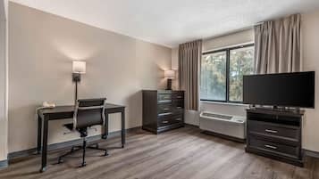 Een hotelkamer met een bureau, stoel, televisie, dressoir en een raam met gordijnen.