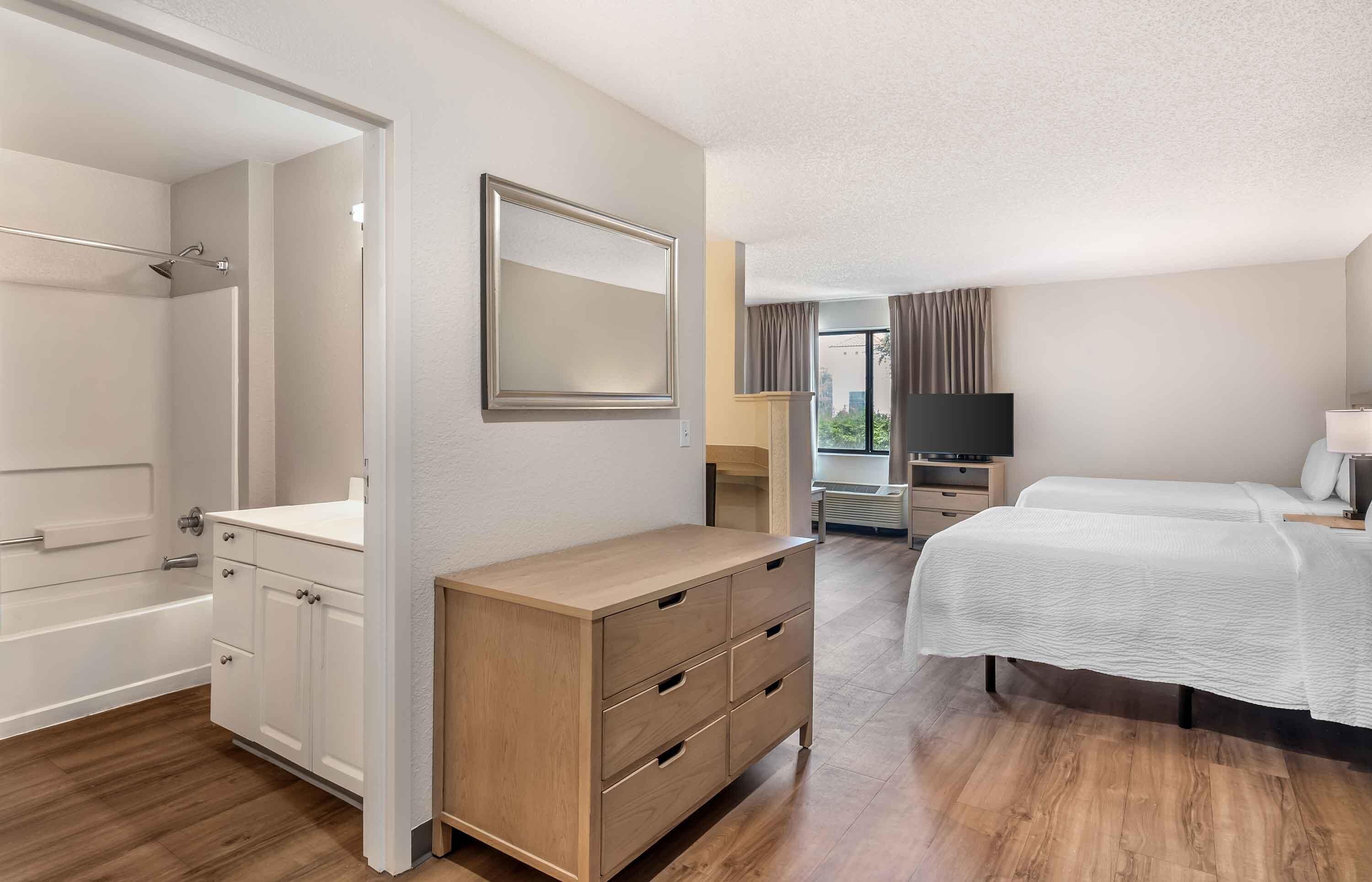 A hotel room with a wooden dresser, a bed, a TV, and a bathroom with a shower and toilet.