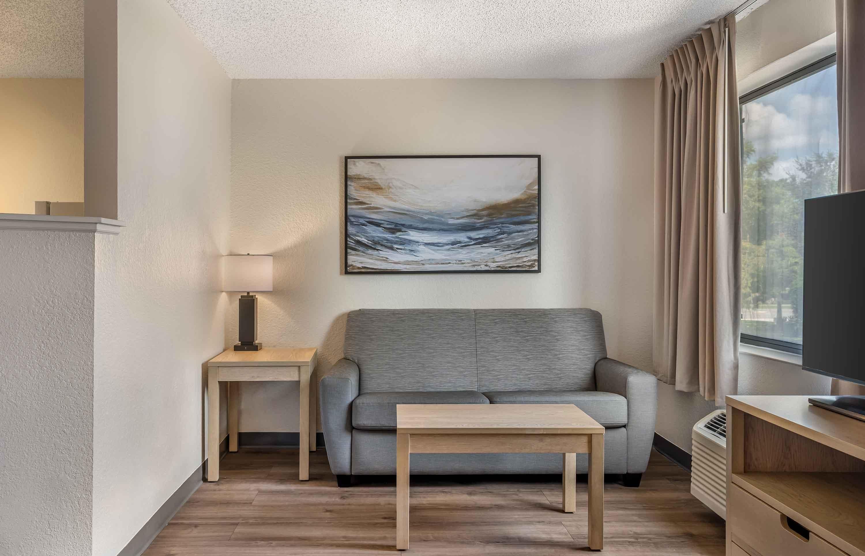 Ein modernes Wohnzimmer mit einem grauen Sofa, einem kleinen Holztisch, einer Lampe und einem Gemälde an der Wand.
