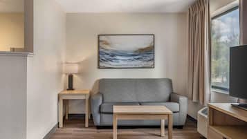 Una sala moderna con un sofá gris, una pequeña mesa de madera, una lámpara y un cuadro en la pared.