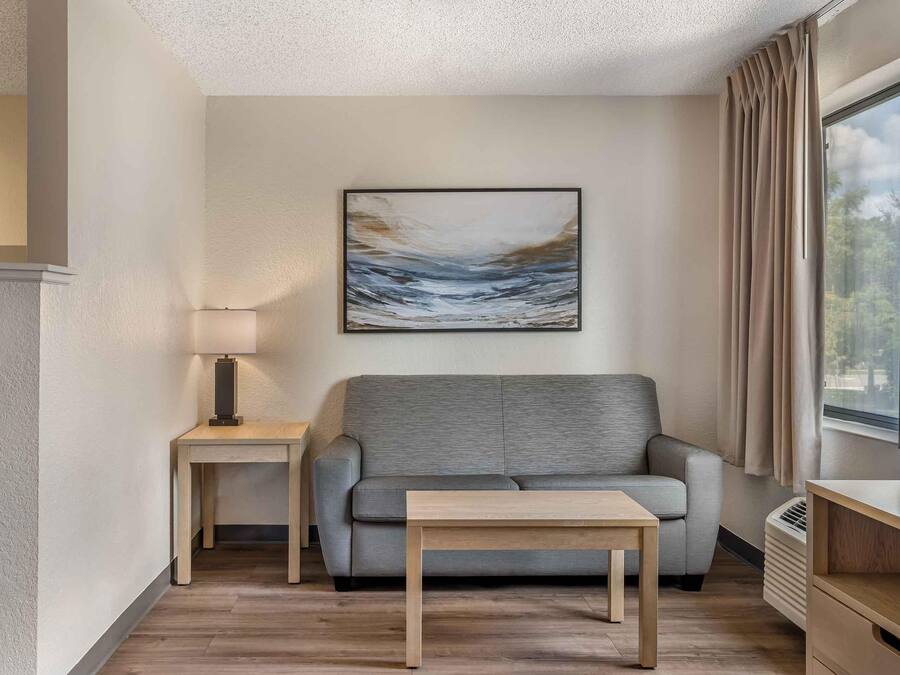 A modern living room with a grey sofa, a small wooden table, a lamp, and a painting on the wall.