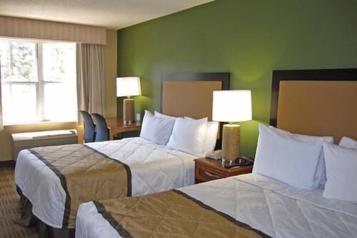 A hotel room with two beds, a nightstand with a lamp, a chair, and a window with curtains.