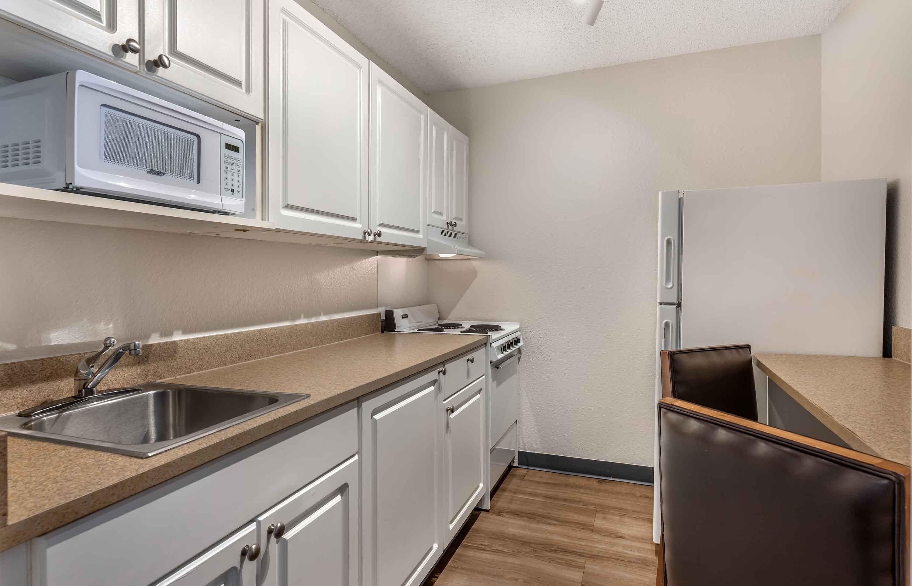 A modern kitchen with white cabinets, a stainless steel sink, a microwave, a stove, and a refrigerator.