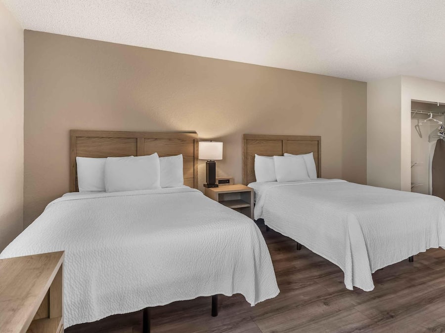 A hotel room with two beds, a bedside table, a lamp, and a wardrobe.
