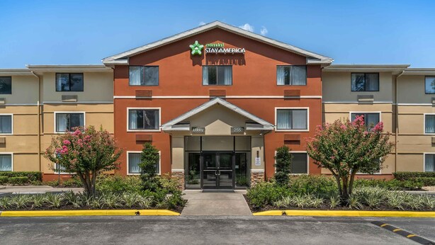 Un hôtel à plusieurs étages, avec une façade rouge, un hall d’entrée et une enseigne indiquant « EXTENDED STAY AMERICA ».