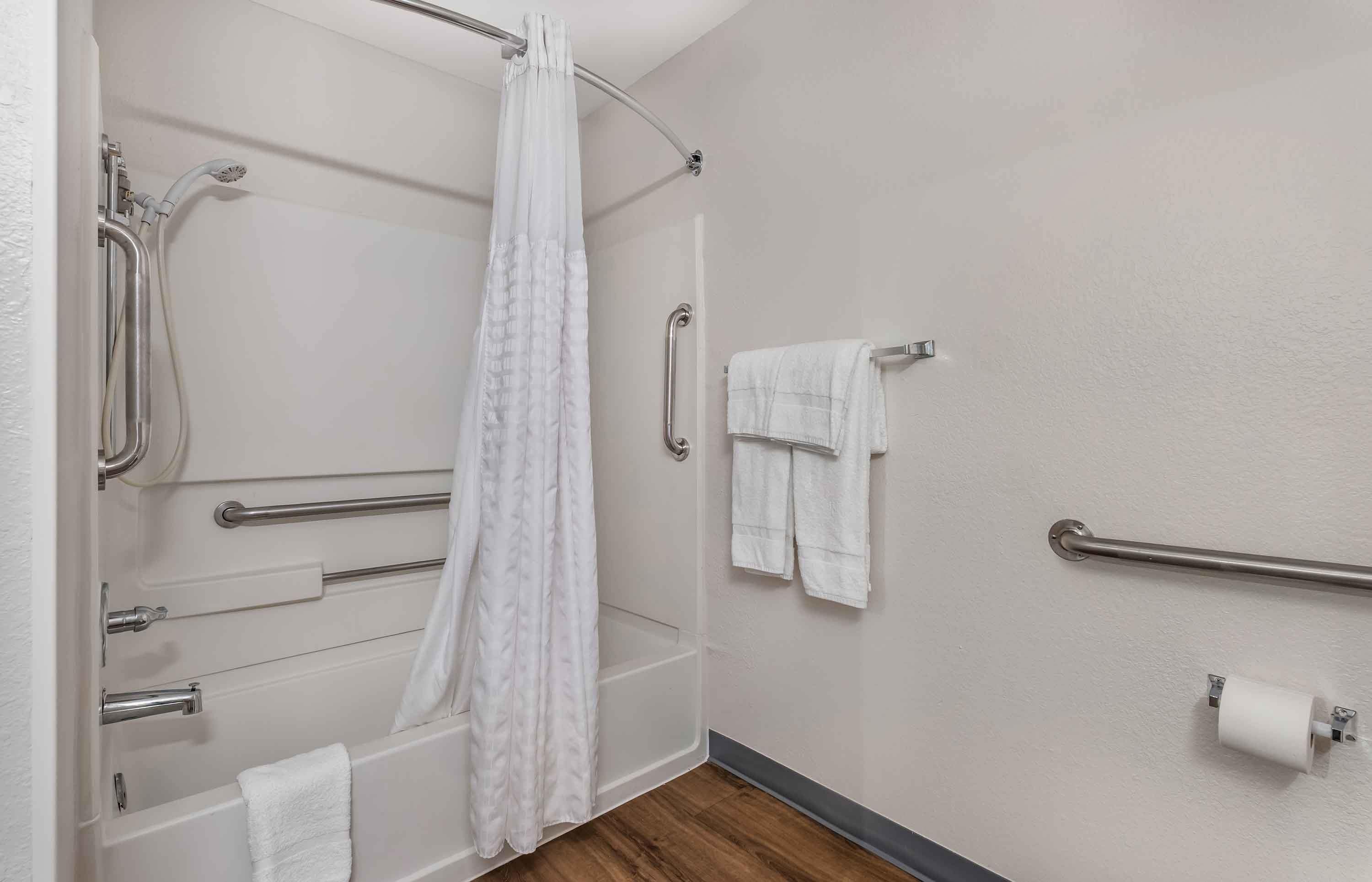 A bathroom with a shower, grab bars, a towel rack, and a toilet paper holder.