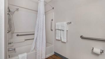 A bathroom with a shower, grab bars, a towel rack, and a toilet paper holder.