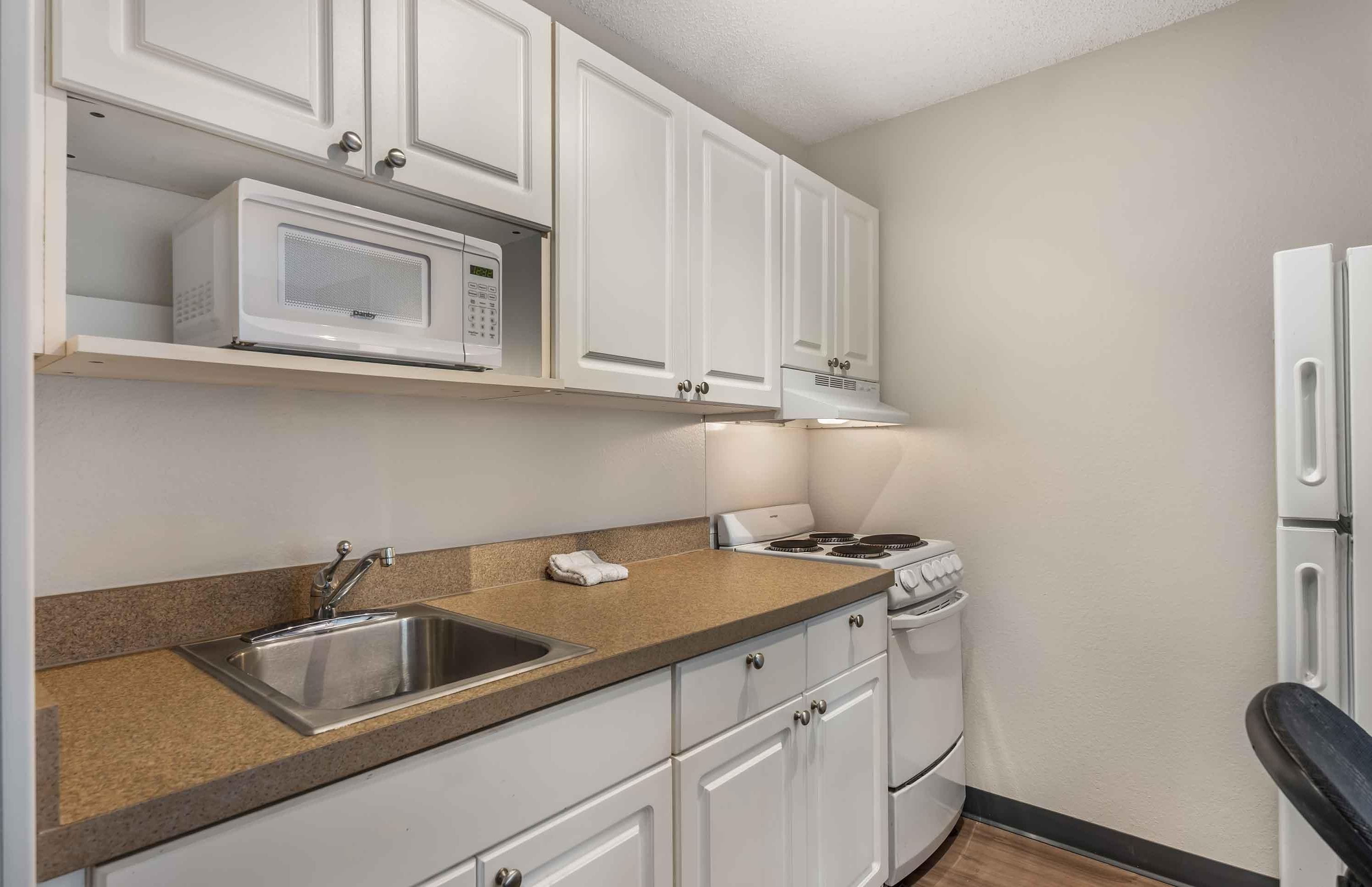 A kitchen with white cabinets, a microwave, a stove, and a sink.