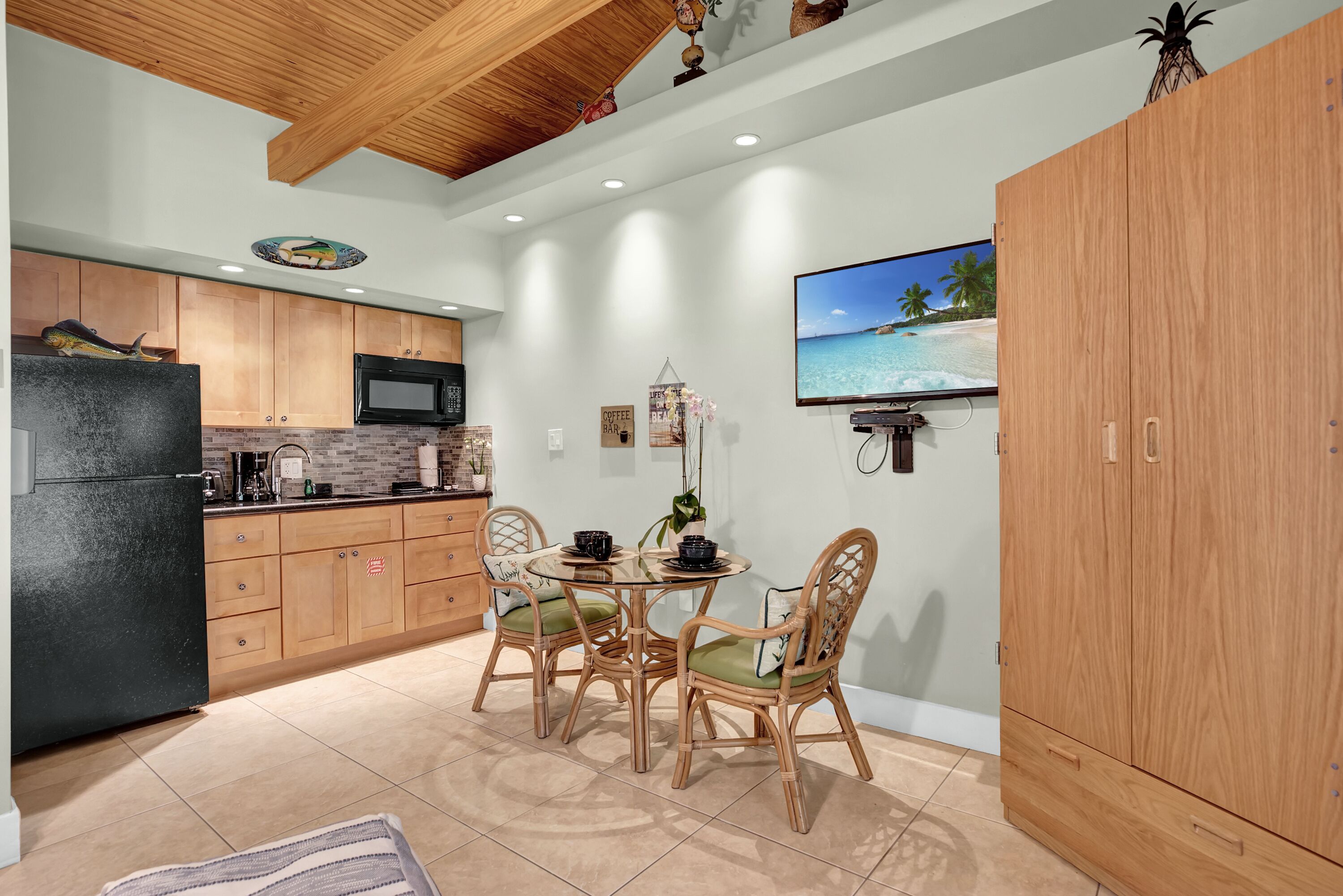 A modern kitchen with wooden cabinets, a black refrigerator, and a dining area with wicker chairs and a round table.