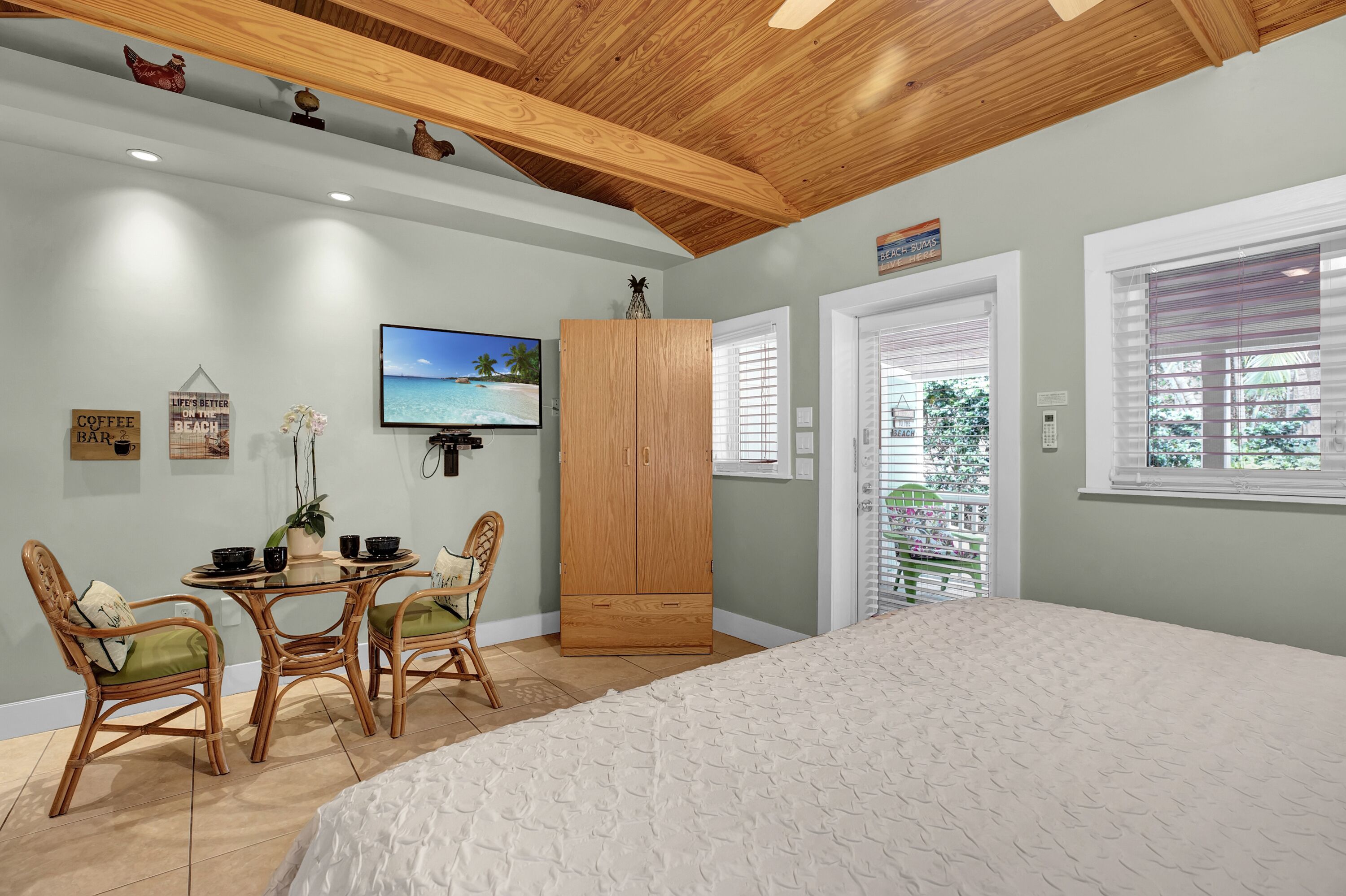 Un dormitorio con una cama grande, un armario de madera, una mesa de comedor con sillas y un televisor en la pared.