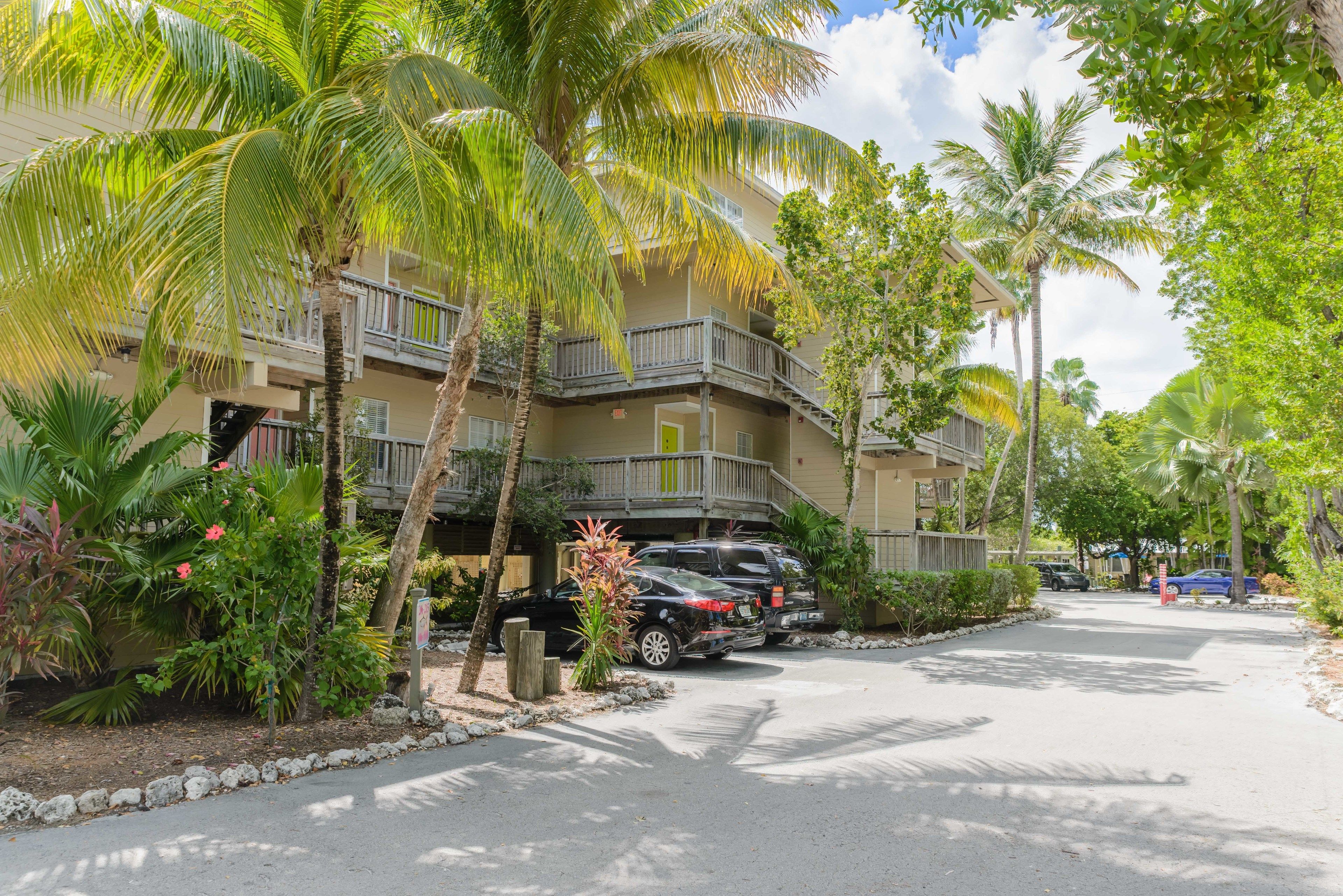 A multi-story hotel with balconies, surrounded by palm trees and parked cars.