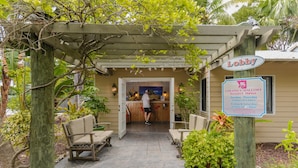 A lobby area with a wooden pergola, outdoor seating, and a sign indicating the Coconut Mall Resort & Marina's operating hours.