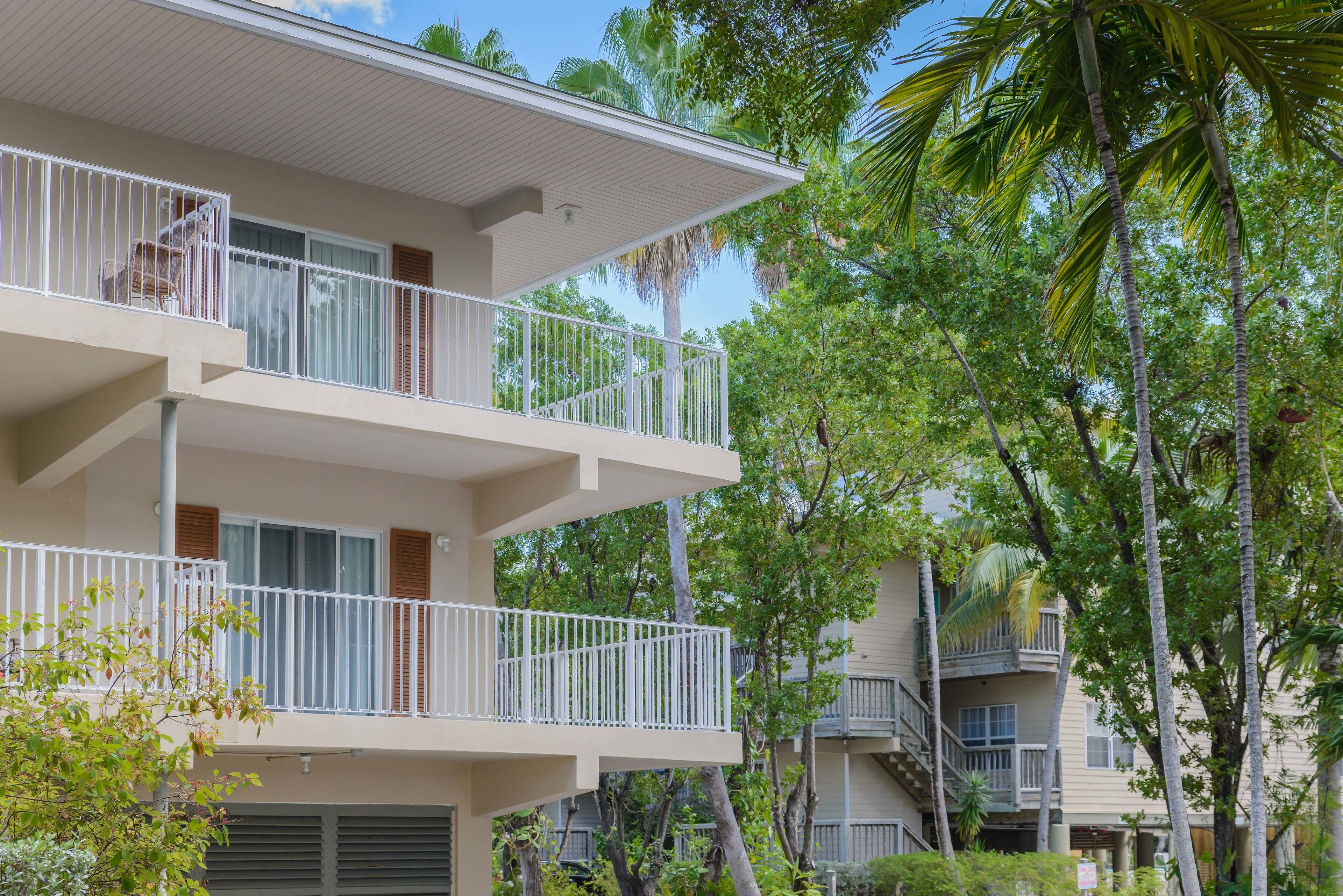 A multi-story residential building with balconies, surrounded by palm trees and other greenery.