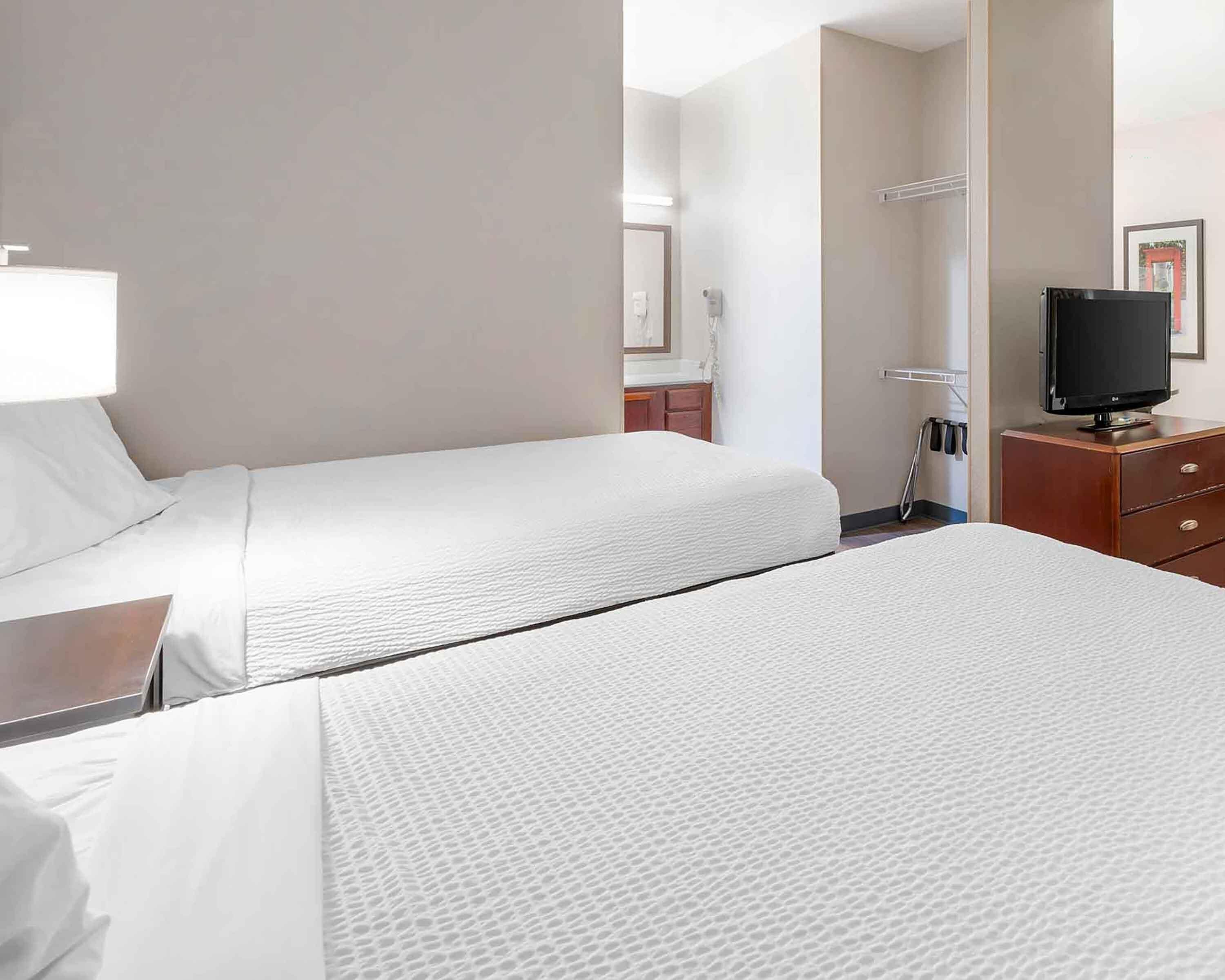 A hotel room with two beds, a TV, a desk, and a mirror.