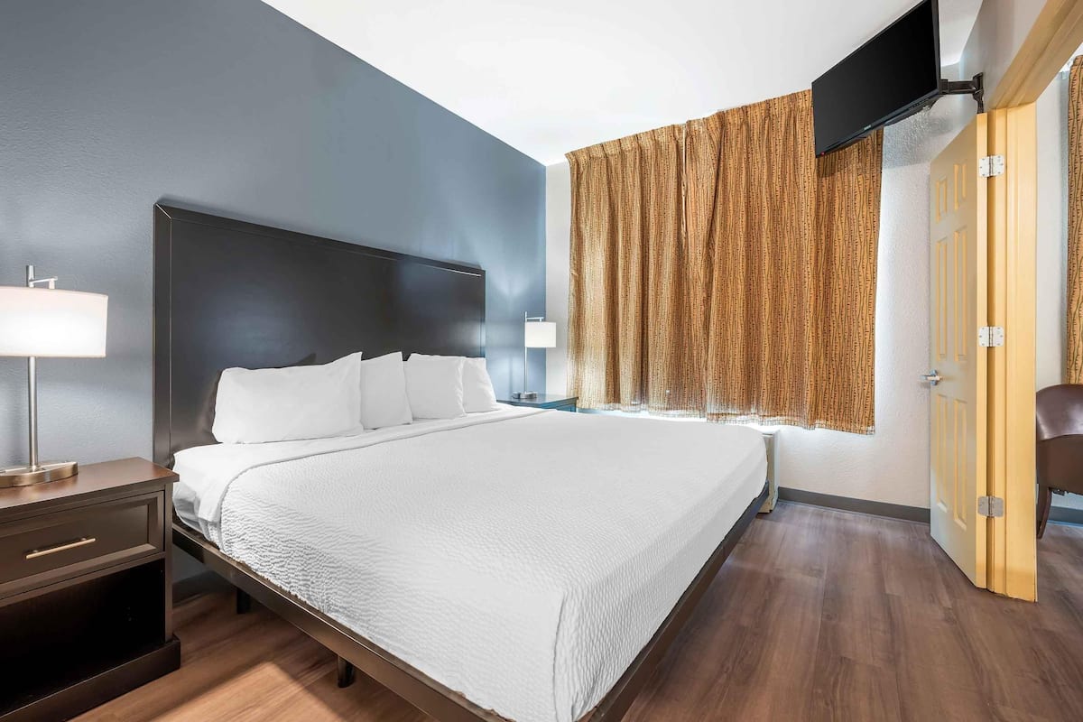 Una camera d'albergo con un letto grande, comodini, una TV a parete e una finestra con tende.