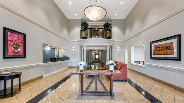 Un hall de hotel con una recepción, una escalera que lleva a un balcón y un letrero que dice 'WELCOME'.