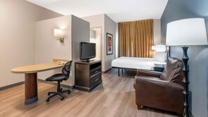 Una habitación de hotel con una cama, un escritorio con silla, televisor, lámpara y un sofá.