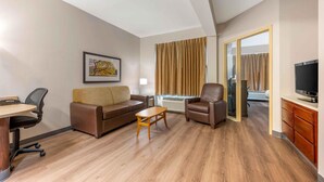 Habitación de hotel con sofá, sillón, mesita, televisión y un cuadro en la pared.